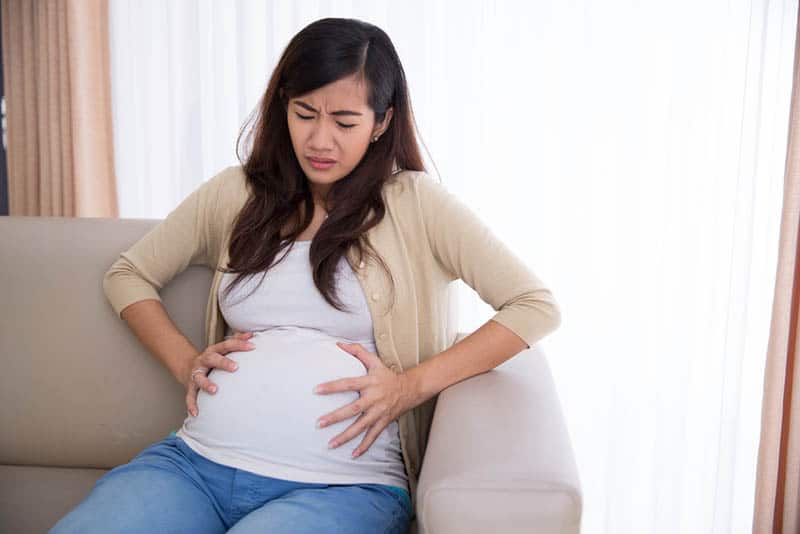 pregnant woman sitting on the couch in pain and holding for belly