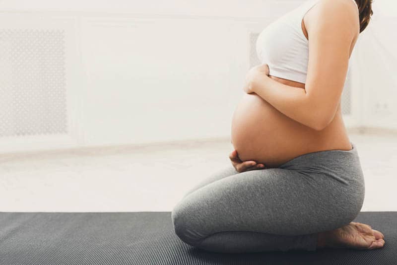 pregnant woman training yoga in hero pose caressing her belly