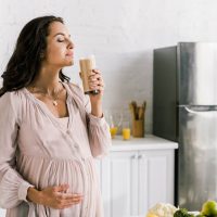 pregnant woman holding a glass of protein shake in the kitchen
