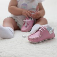 baby girl sitting on floor and playing with pink shoes