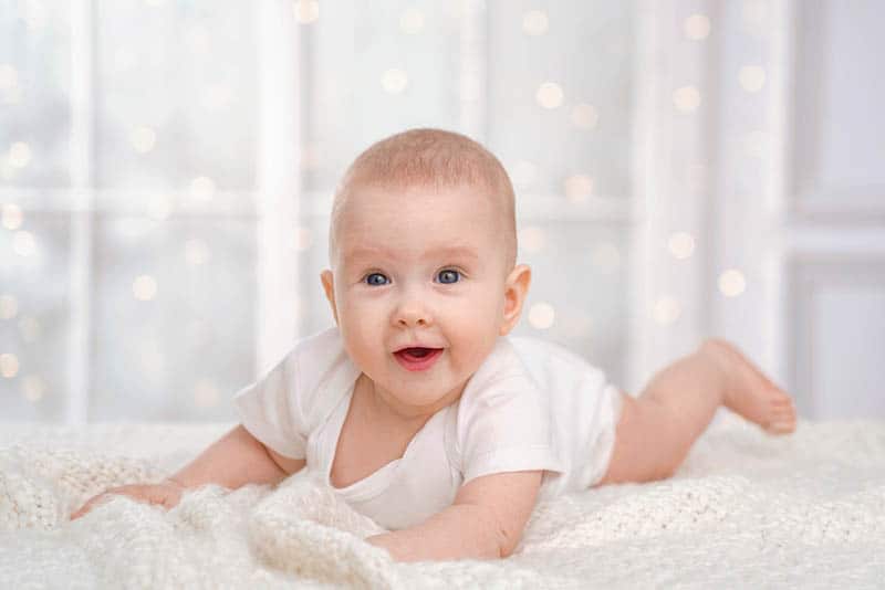 smiling baby lying on tummy on the bed with lights behind