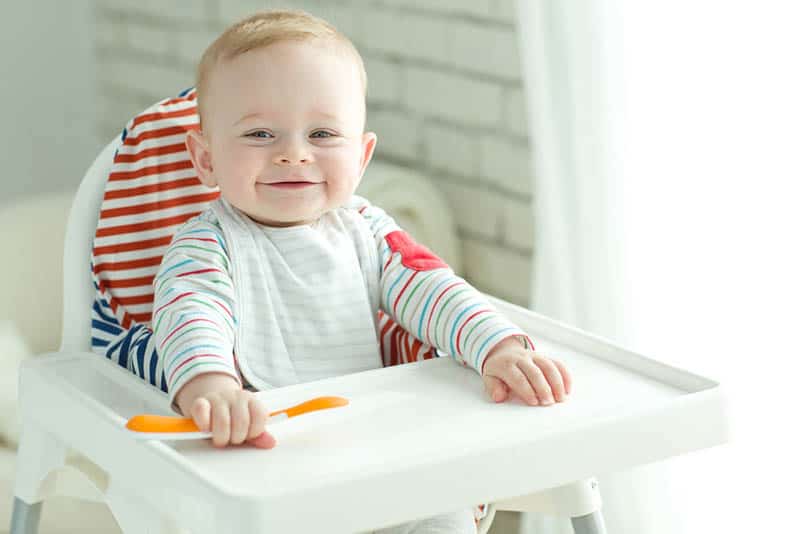 smiling baby sitting in high chair and waiting for food