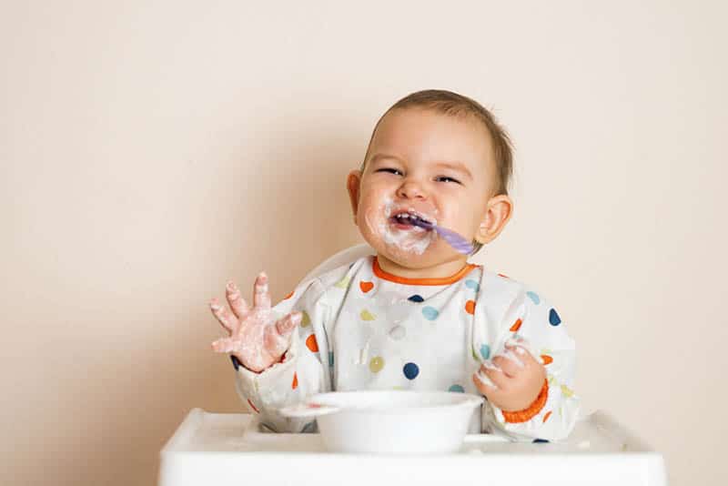 smiling baby wearing a bib with sleeves and making a mess while eating