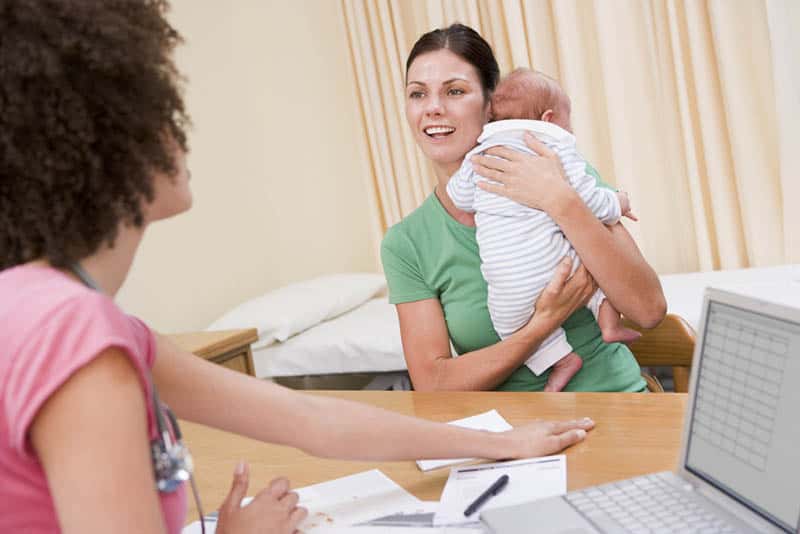 smiling mother holding baby and talking to a female doctor in the hospital 