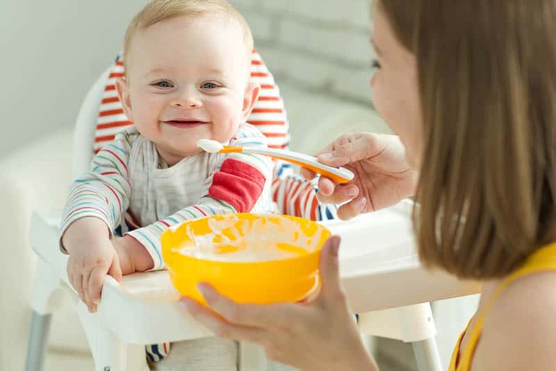 smiling mother trying to feed smiling baby in high chair