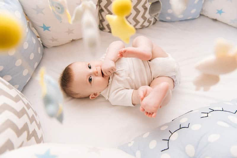 sweet baby in diapers lying in crib and watching toys 