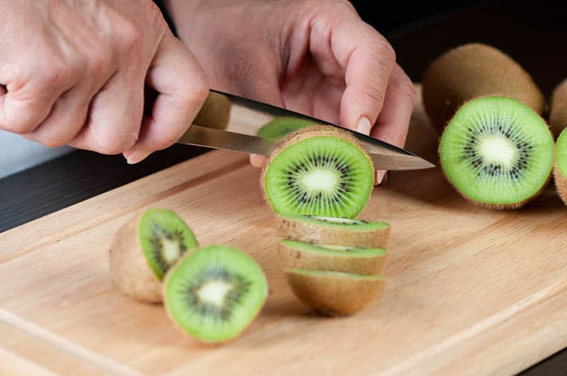 woman cutting kiwi on the wooden cutting board
