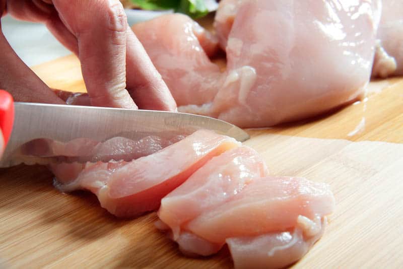 woman cutting raw chicken breast on the wooden board