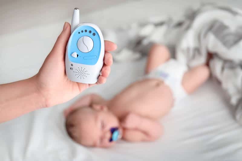 woman holding baby monitor while baby sleeps on the bed
