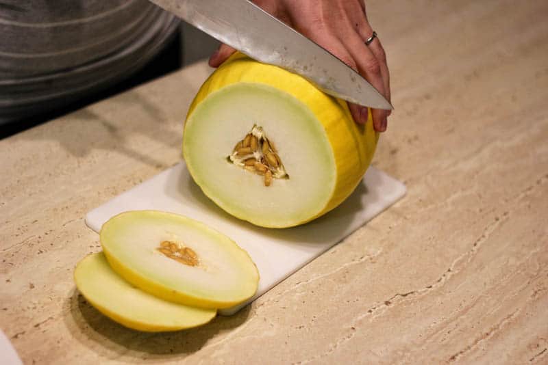 woman slicing a yellow melon with seeds inside on the wooden board