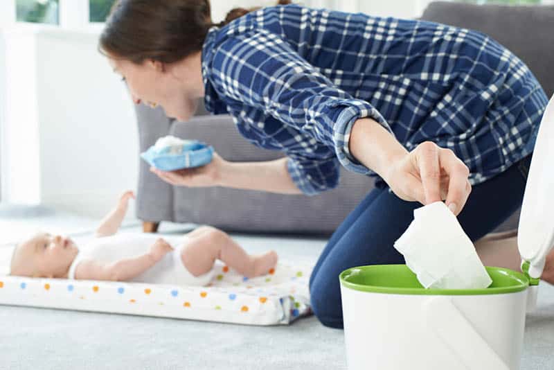 woman smiling to baby and throwing a wipe into the bin in the bedroom