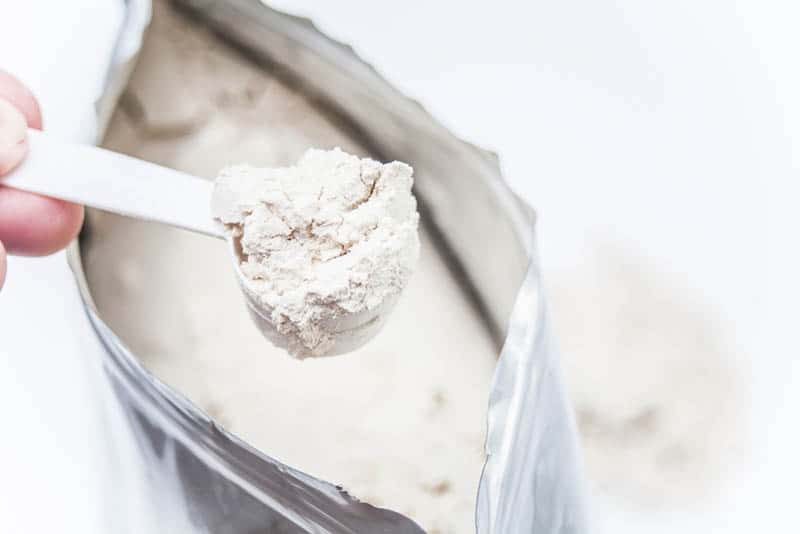 woman's hand holding a spoon of protein powder above the protein package