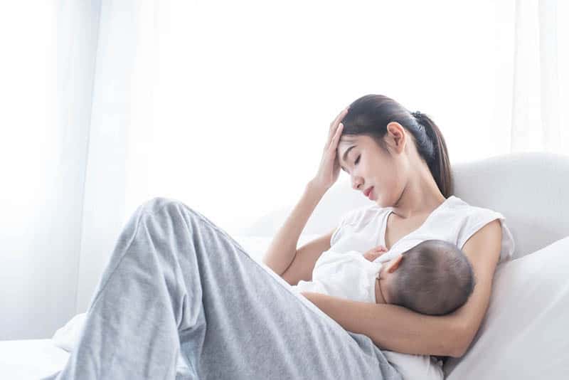 worried woman lying on a bed and trying to breastfeed her baby