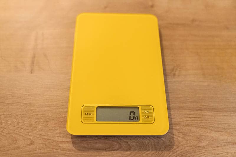 yellow kitchen scale showing 0g at display on the wooden table