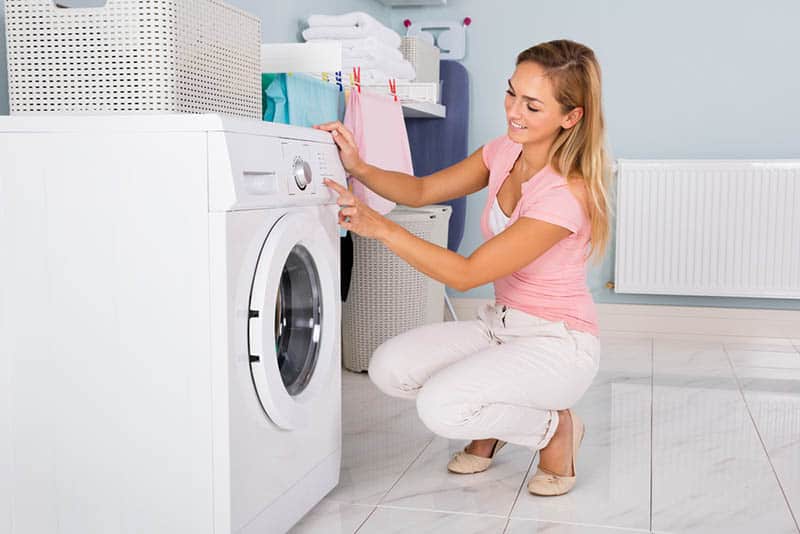 young happy woman using washing machine in the bathroom