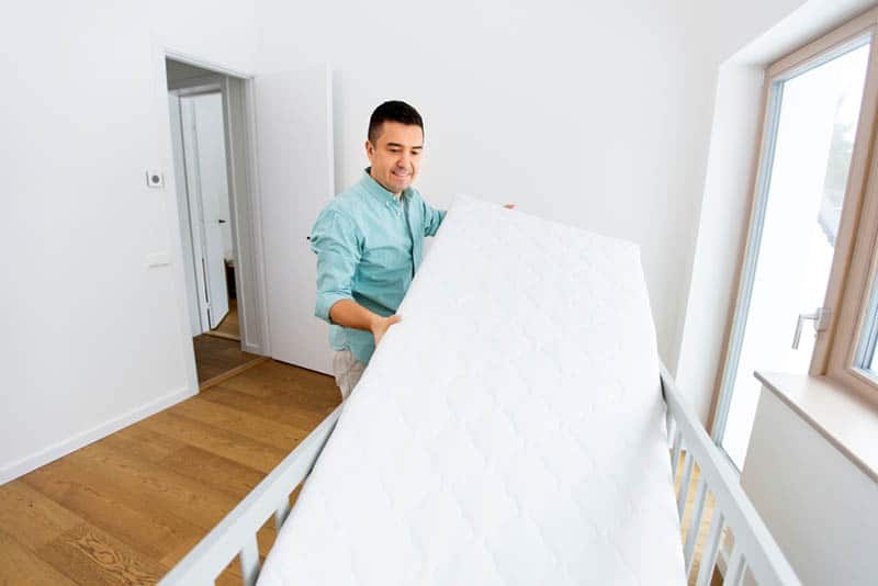 young man putting mattress in baby bed in the room at home
