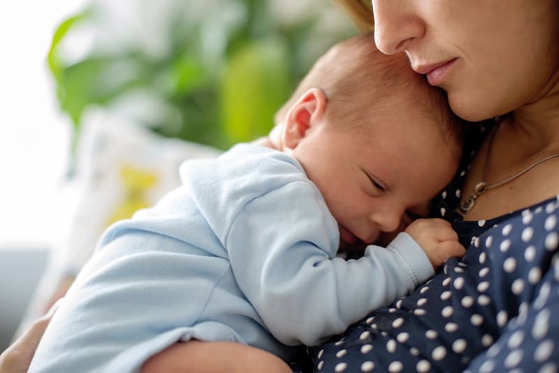 young mother holding her sleepy newborn baby on the chest