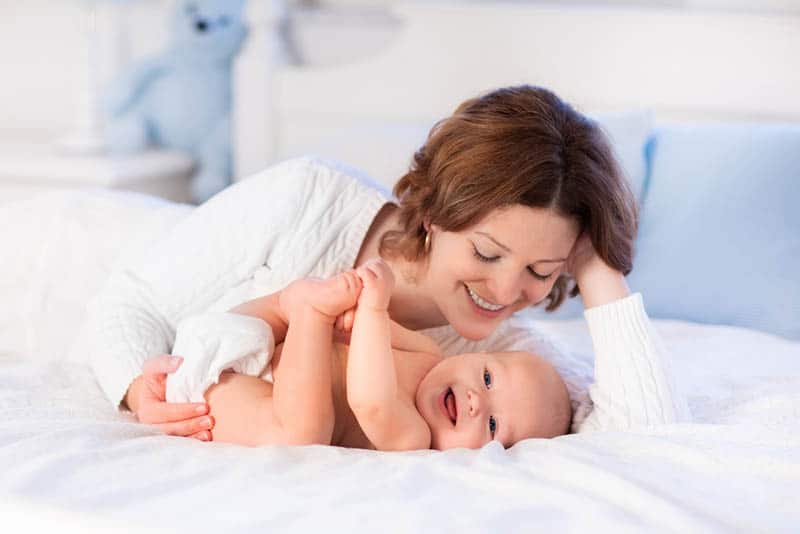 young mother playing with smiling baby in diaper on the bed