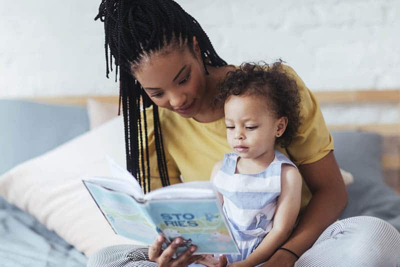 young mother reading a book with her cute little daughter on the bed