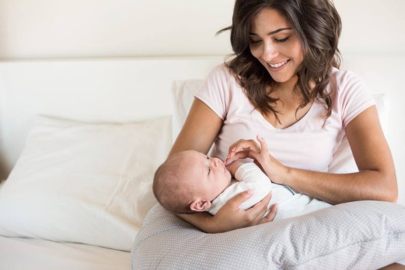 young smiling mother holding her baby in arms on the big pillow support