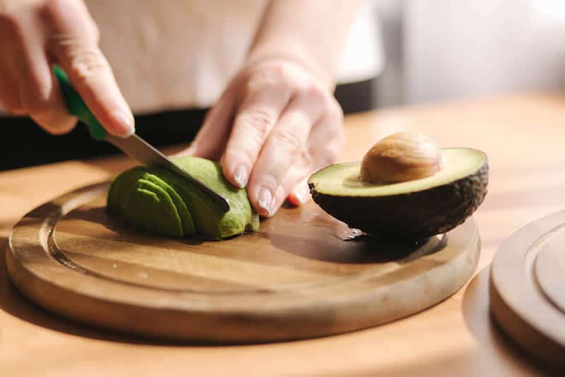 young woman cutting an avocado on the wooden board on the table