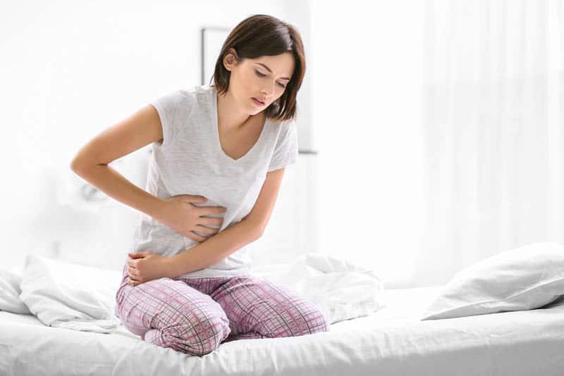 young woman feeling big pain in abdominal area while sitting on the bed at home