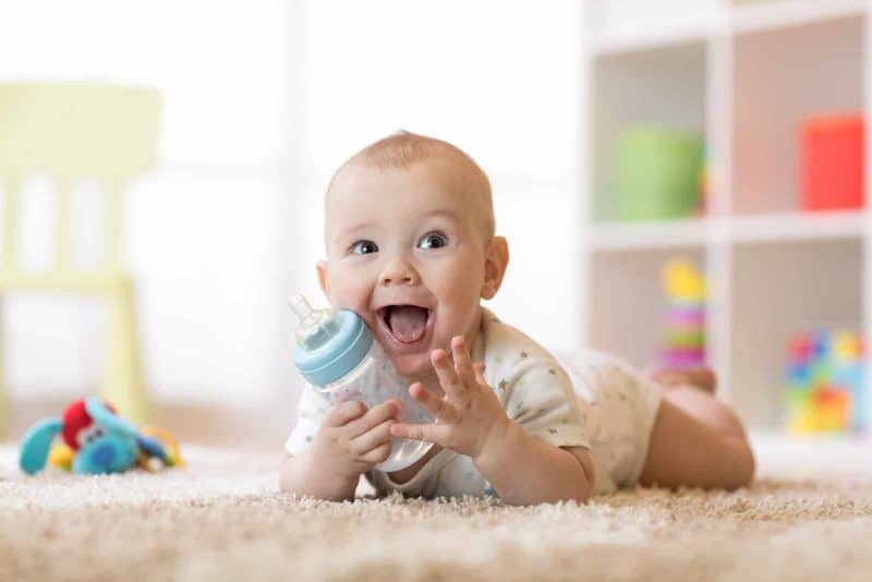 baby boy laughing while holding a bottle on the floor