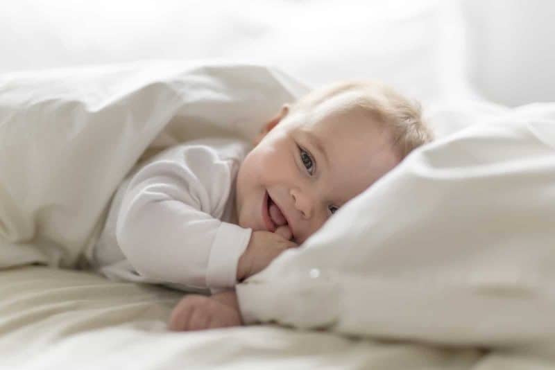 smiling baby lying in the bed and chewing on her fingers