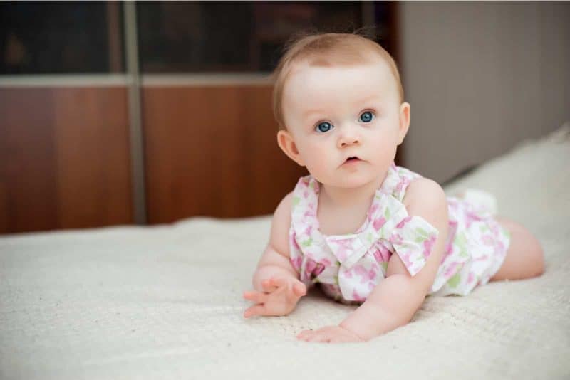 beautiful baby girl with big blue eyes lying on the bed