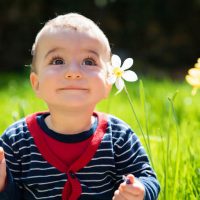cute baby boy playing with flower in the meadow
