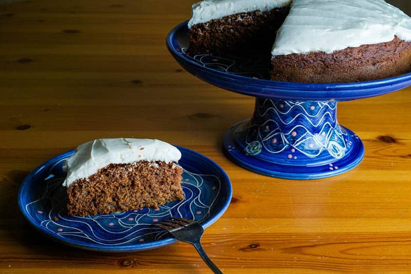 Applesauce cake with cream cheese frosting on the blue stand on the table