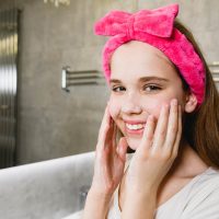 teen girl with pink headband washing her face