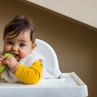 sweet baby in a high chair eating a cucumber