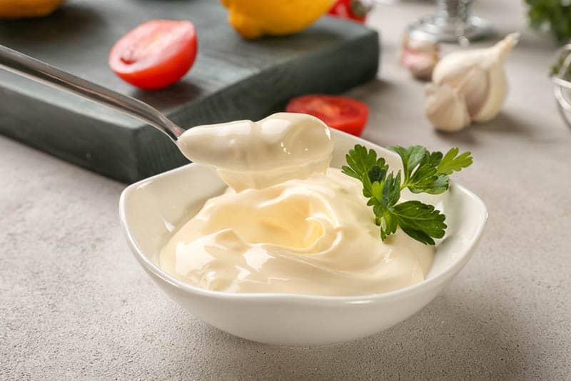 Delicious mayonnaise in bowl and spoon on kitchen table