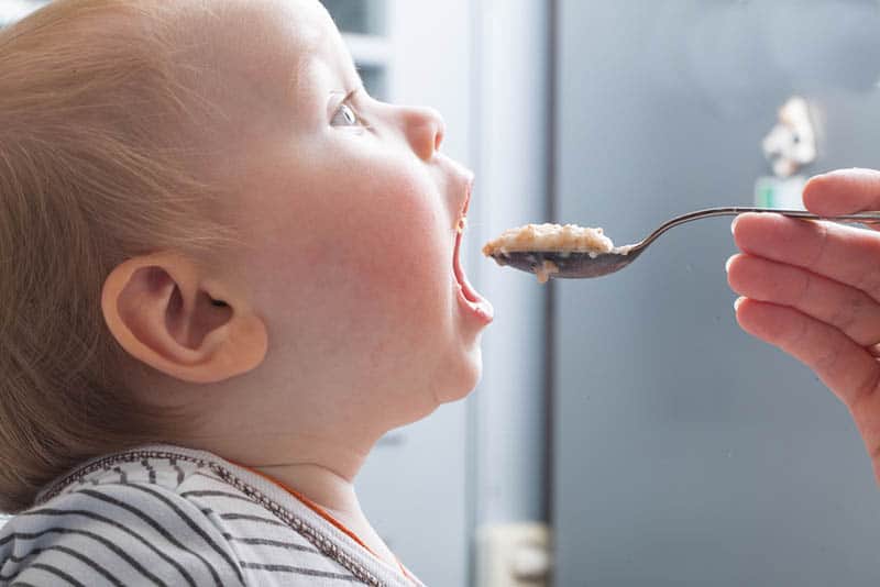 Mother feeds baby boy with a spoon porridge