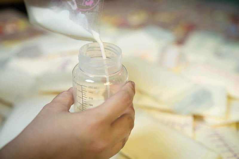 Mother is pouring milk from breast milk storage bags to baby bottle with measuring scale