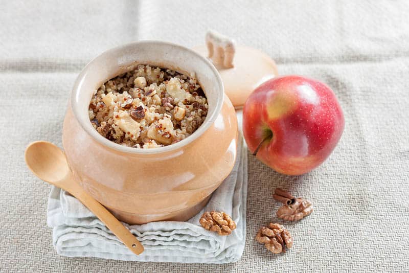 Quinoa porridge with apples, walnuts, cinnamon and cheese in a pot on the cloth