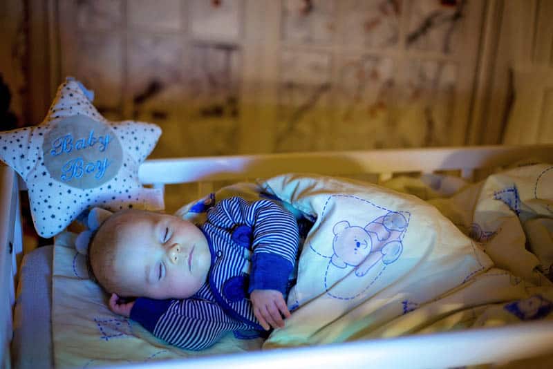 adorable baby boy sleeping in a bassinet covered with blanket in bedroom