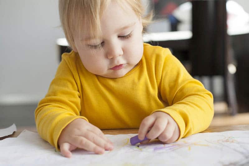 adorable baby girl sitting by the table and drawing on white paper