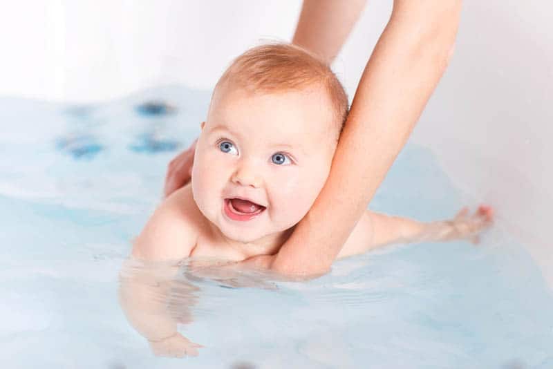 adorable baby with blue eyes taking bath by mother