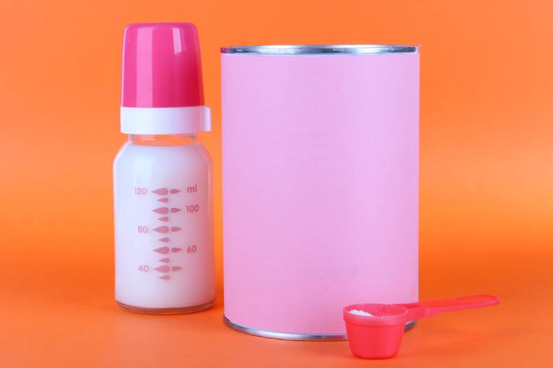 baby bottle and baby formula can on orange background
