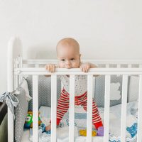 cute baby girl standing in the crib and chewing on the rail