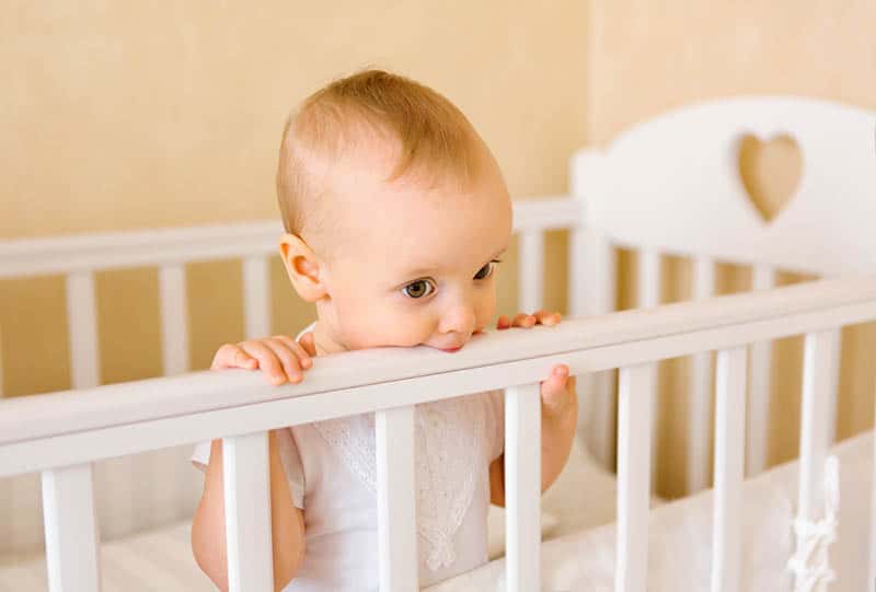baby girl standing in the crib and chewing rail