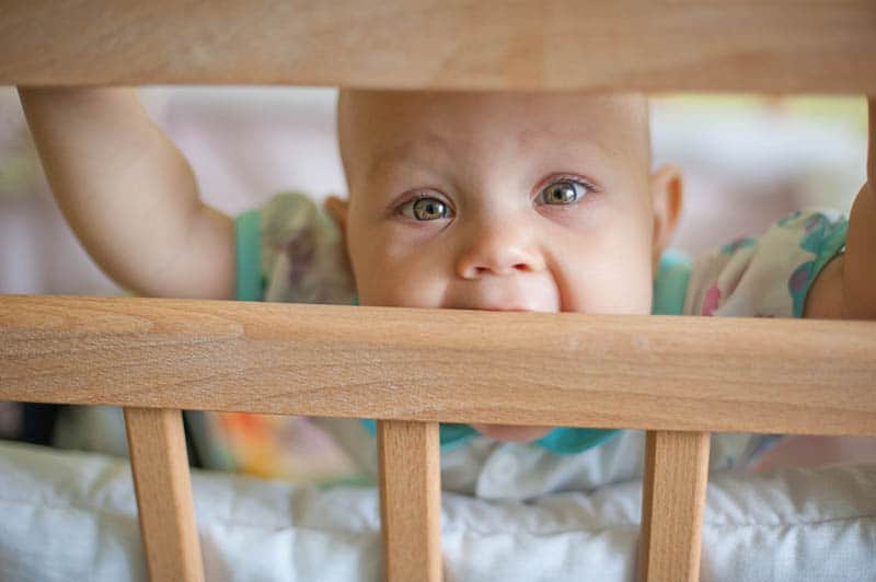 baby girl with wonderful eye color chewing crib rails