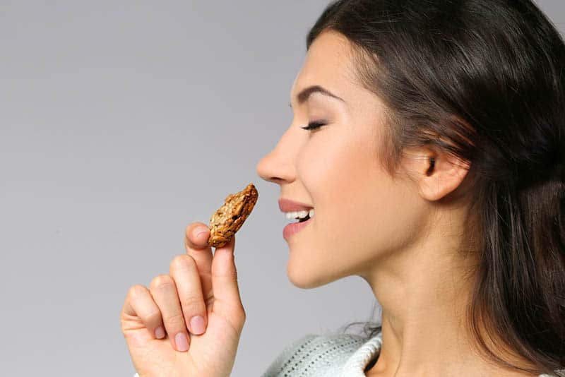 beautiful young woman holding a cookie to eat with closed eyes