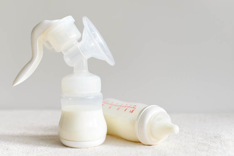breast pump with milk and a bottle with milk on the white table