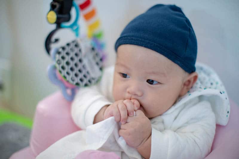 cute baby boy with hat taking cloth to mouth