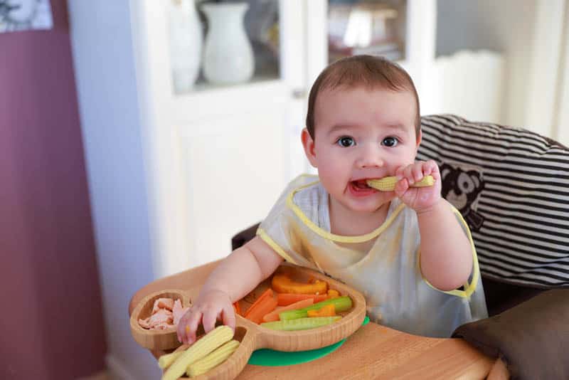 cute baby girl eating vegetables in high chair