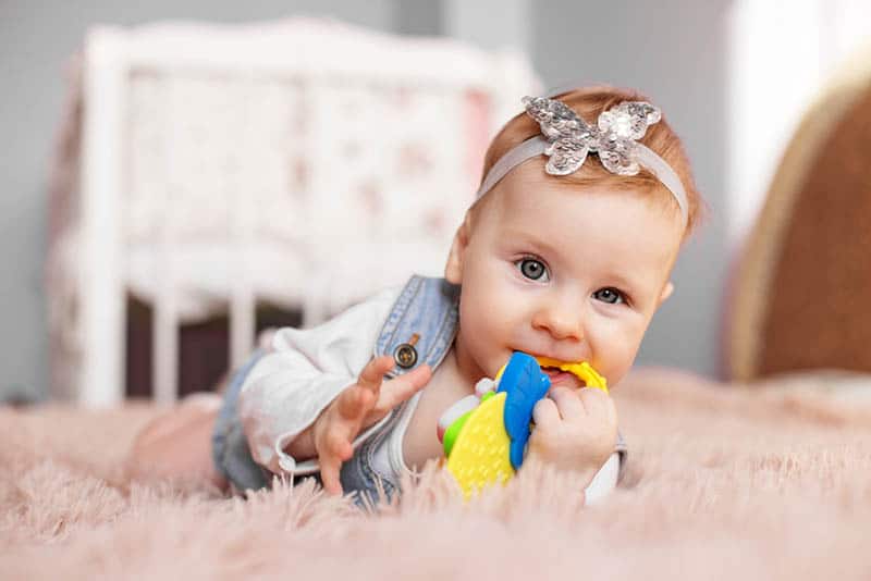 cute baby girl lying on the floor and chewing a teething toy