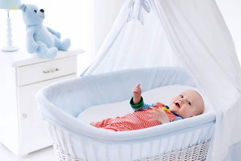 cute baby in colorful pijama lying in the white bassinet in the baby room